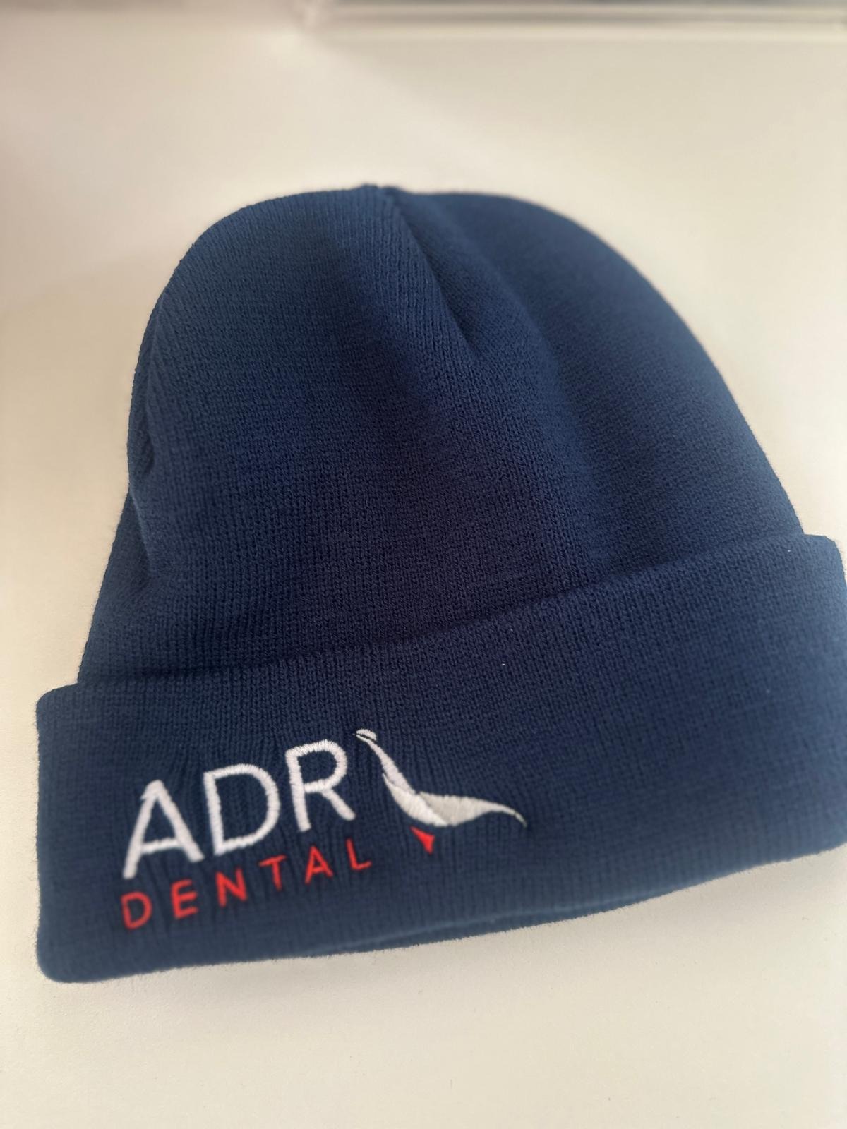 Navy blue beanie with ADR Dental and a white bird logo, inspired by a real Client Story.