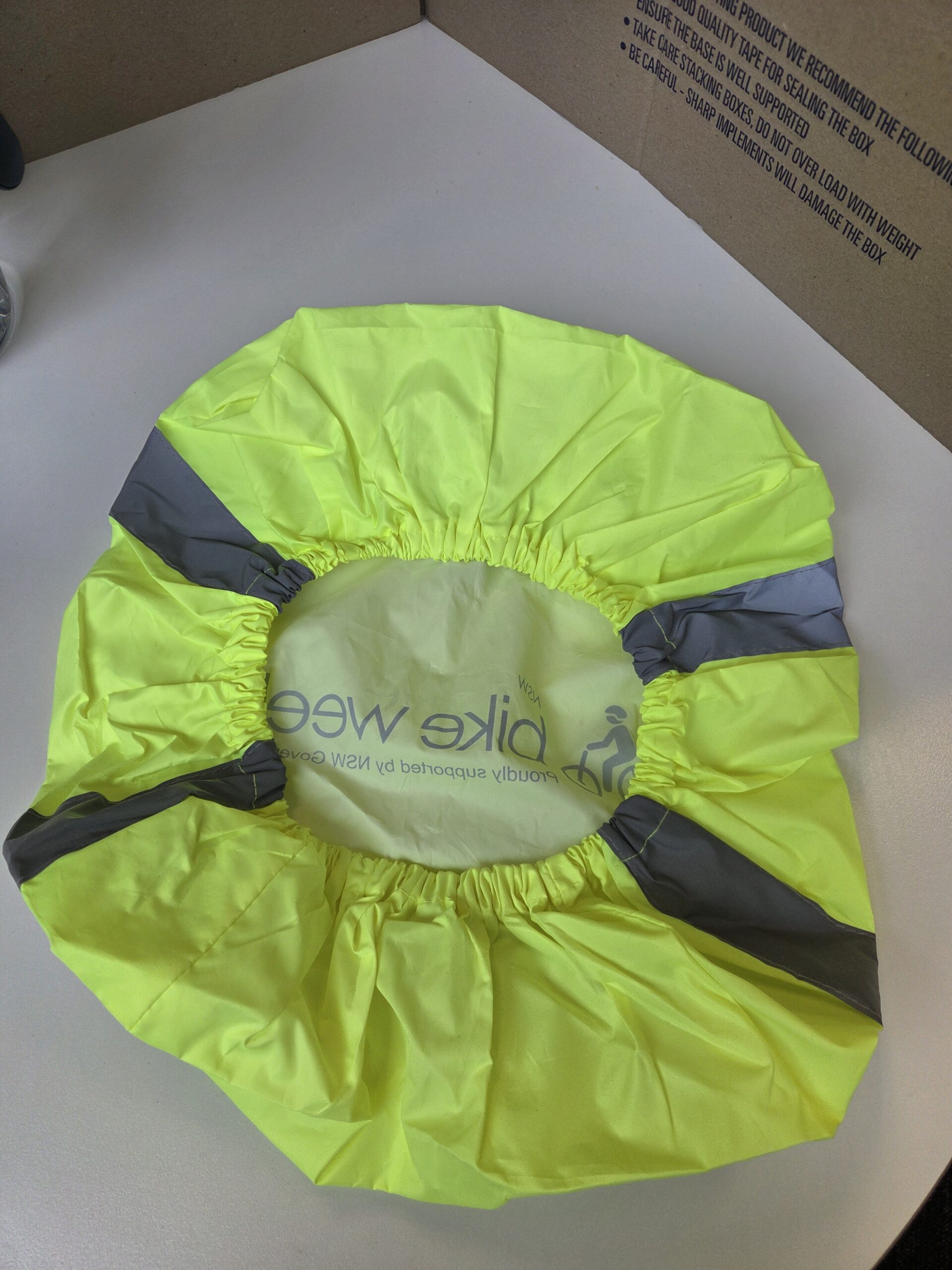 Bright yellow bike wheel cover for Bike Week, with gray reflective strips on a white surface.