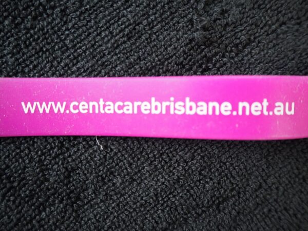 A pink wristband with www.centacarebrisbane.net.au printed on it, on a black fabric.