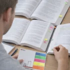 Person studies with books, a notebook, and Combination Sticky Notes on a wooden desk.