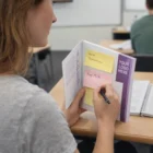 Person writes Buy Milk on Sticky Notes Combo B; Quiz Tomorrow also appears in the notebook.