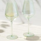 Two transparent wine glasses, one partially filled with white wine, on a light surface.