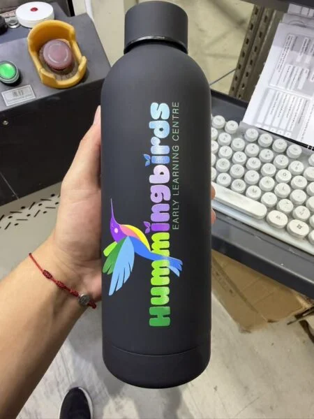 A black bottle with a colorful hummingbird logo and Hummingbirds Early Learning Centre branding.