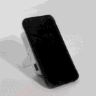 A smartphone rests upright against a small white rectangular object with a stand.