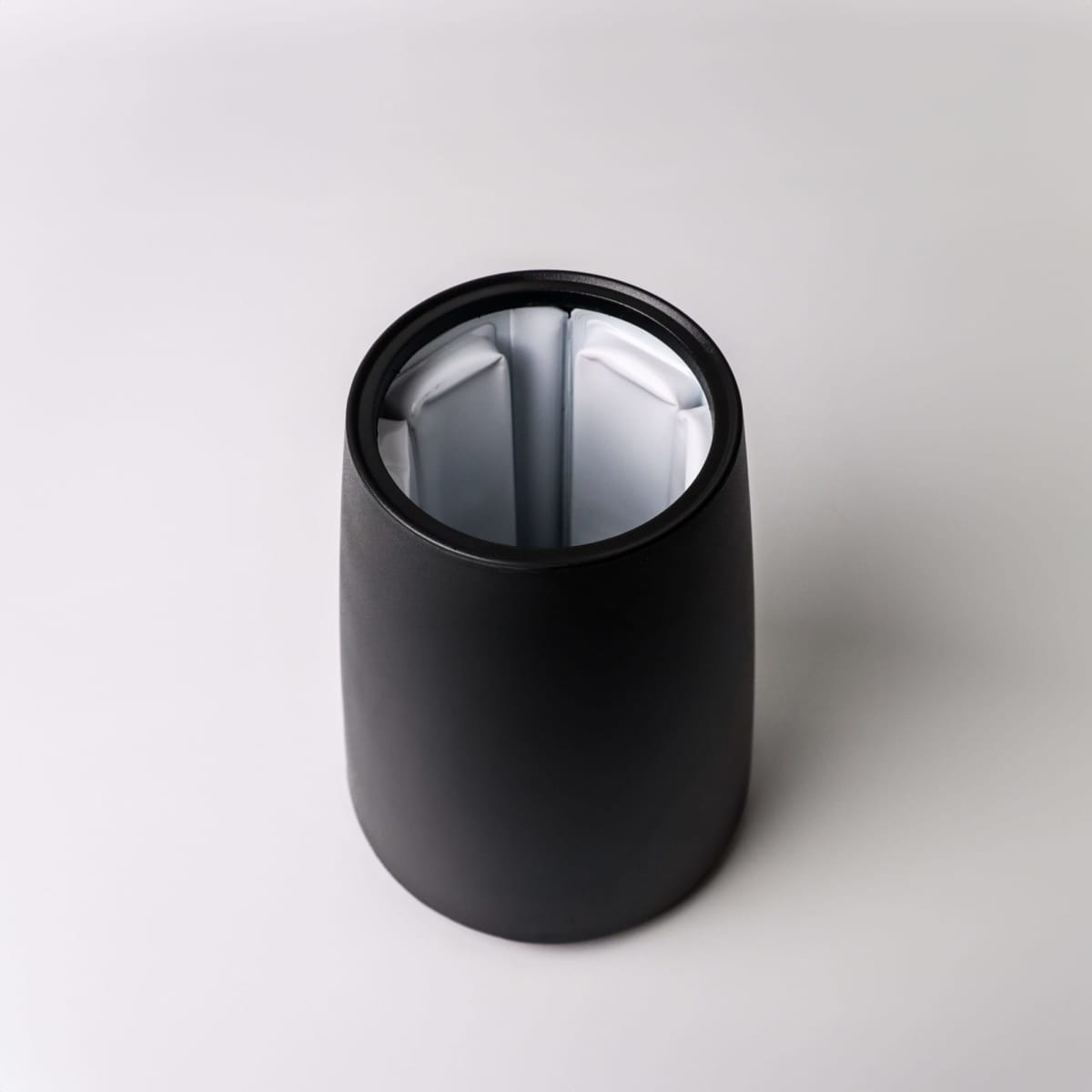 Black, cylindrical container with a divided interior, photographed from above on a white background.