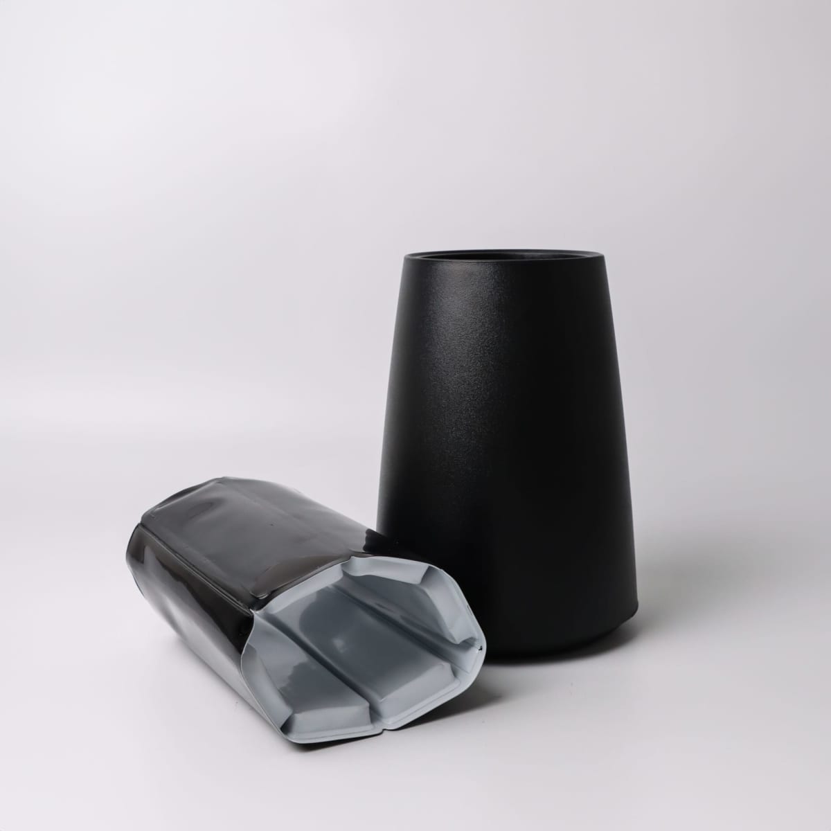 Two black, angular cups; one standing upright and one lying on its side on a white surface.