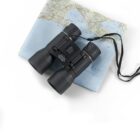 Black binoculars with a neck strap resting on a folded map on a white background.