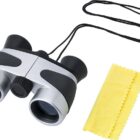 Black and silver binoculars with a neck strap and a yellow cleaning cloth beside them.