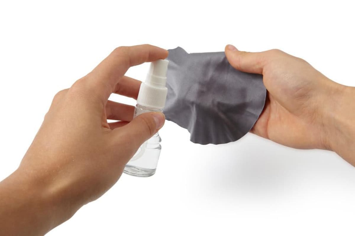 impr_926464.jpg Hand spraying cleaning liquid onto a gray cloth against a white background.