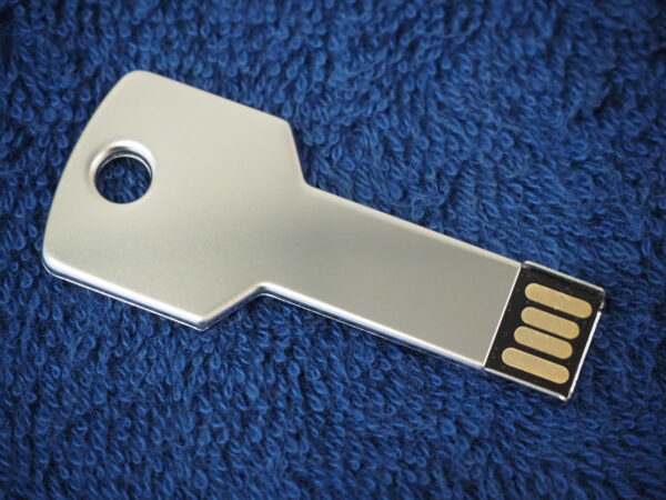A key-shaped USB flash drive resting on a blue textured fabric.