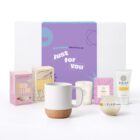 Gift box with a mug, candle, chocolate, marshmallows, lotion, and bath products displayed.