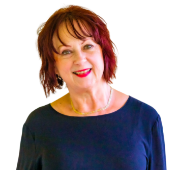 Meet the team: Smiling older woman with short red hair, navy top, and gold necklace.