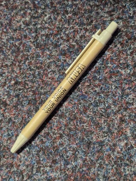 Tan pen labeled INUSA on a multicolored textured carpet, perfect for conference merchandise.