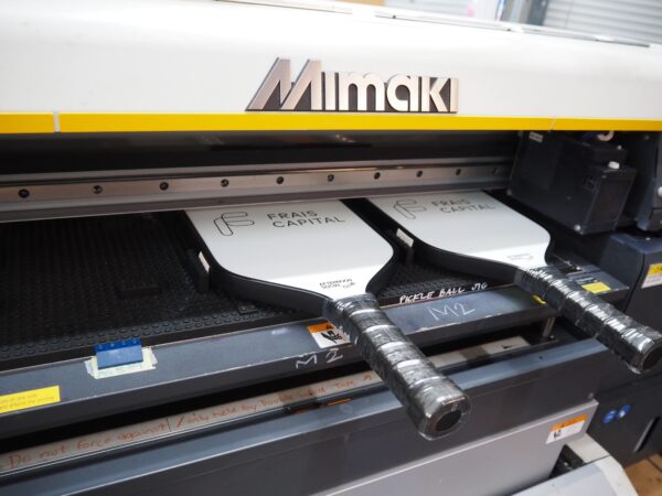 Two pickleball paddles, compatible with various print methods, being printed in a Mimaki machine.