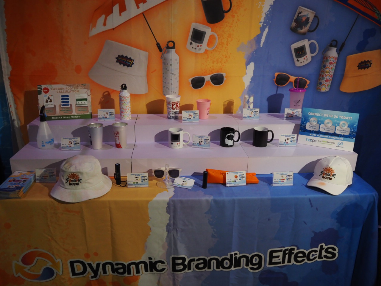 Display table for Large Event Order with branded mugs, bottles, hats, and sunglasses.