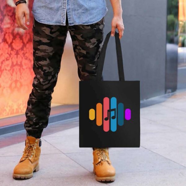 Person holding a black tote bag with a colorful music note and soundwave design.