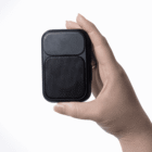 A hand holding a small, black, rectangular portable speaker against a white background.