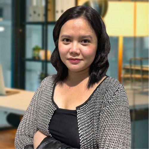 Meet the team: Woman with dark hair in an office, wearing a black top and patterned cardigan.