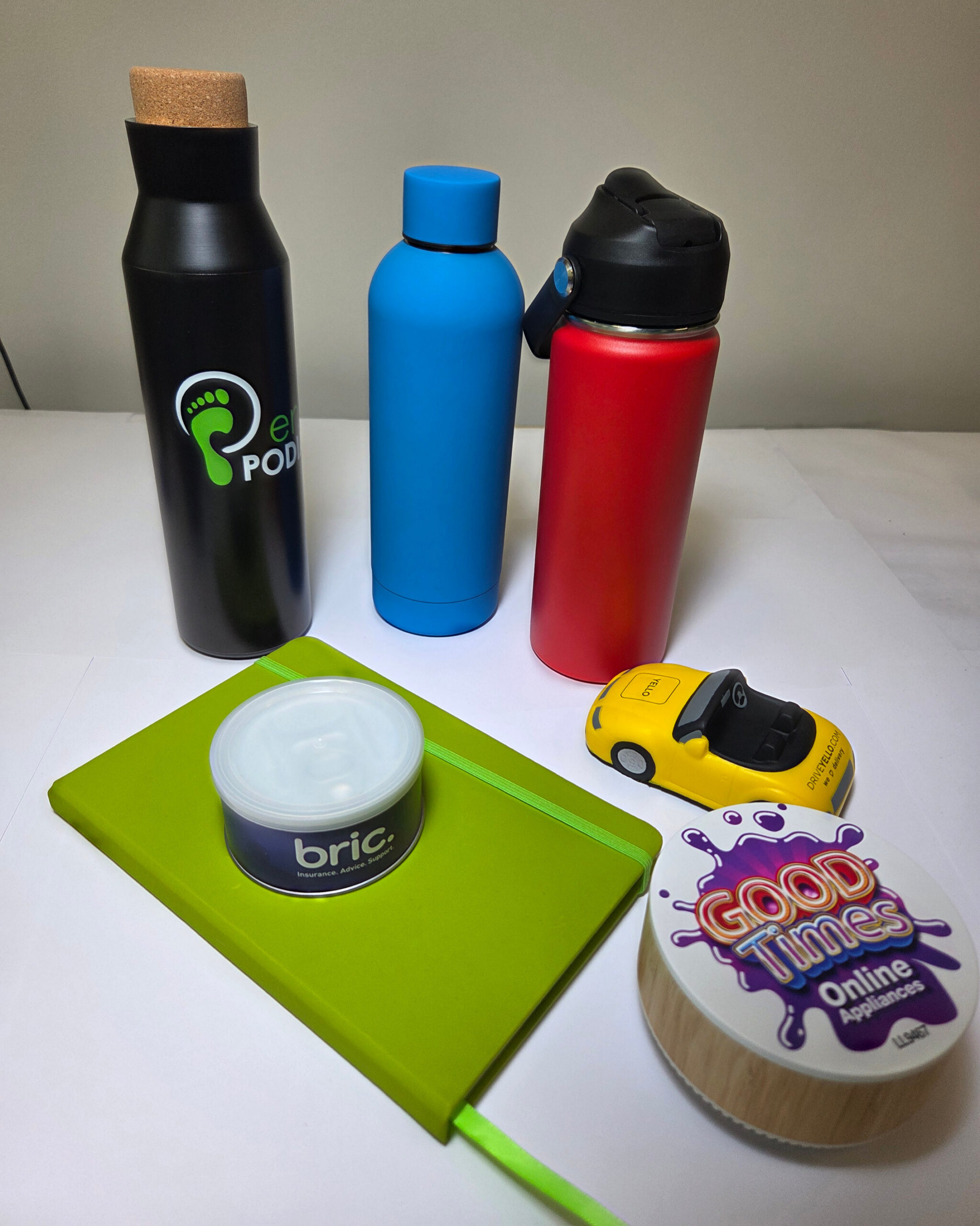 Three bottles, a green notebook, toy car, and tradeshow swag on a white surface.