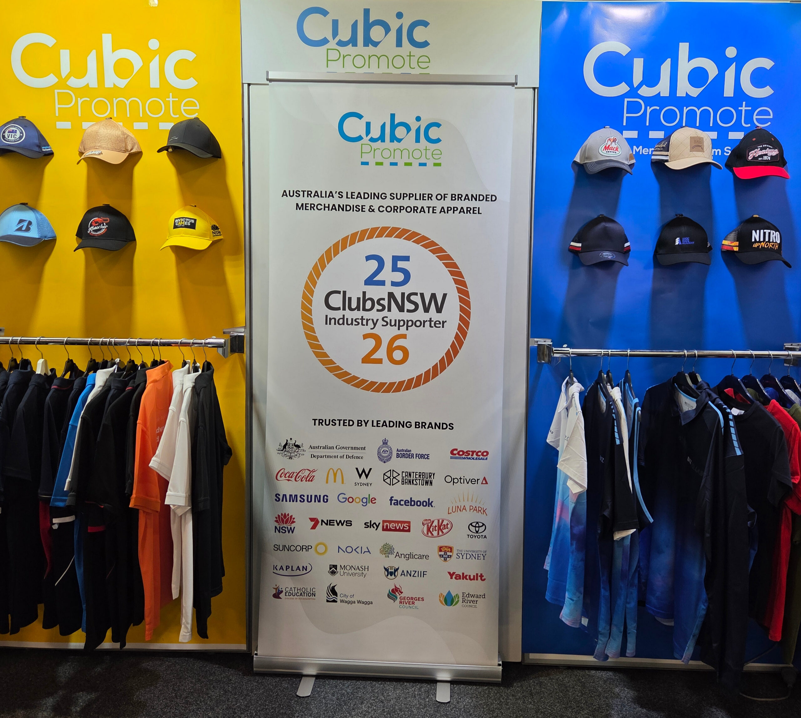 Pop-up display of branded apparel and hats with a Cubic Promote banner and partner logos.
