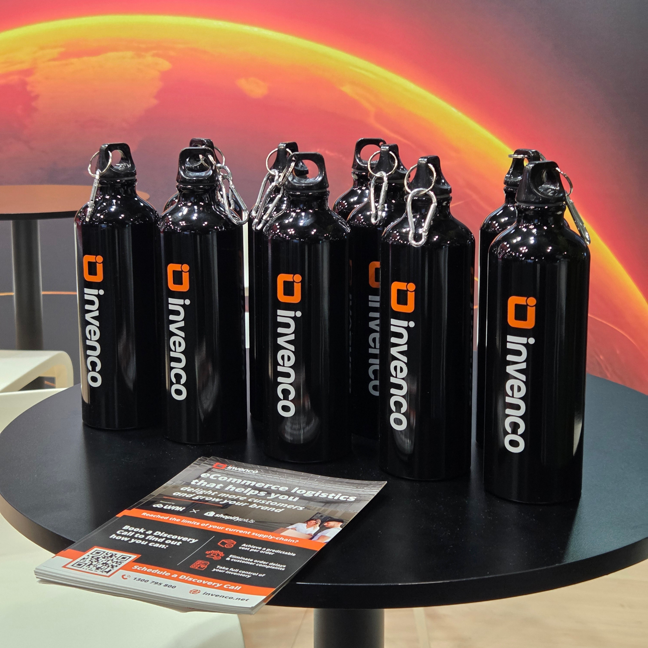 Six Invenco water bottles as promotional products for tradeshows on a round black table.