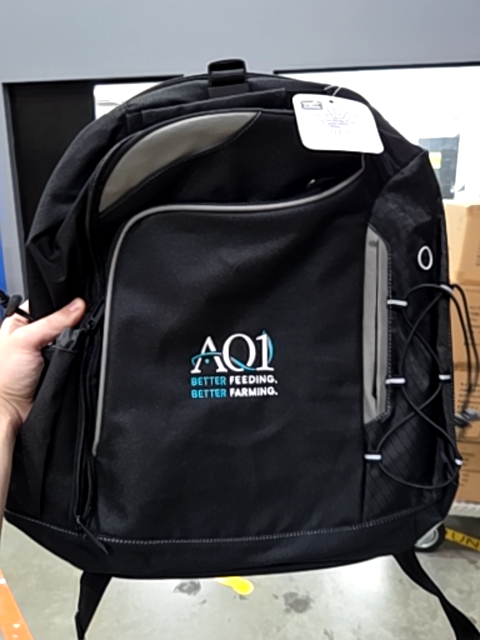 A black backpack with AQ1 Systems and BETTER FEEDING. BETTER FARMING. logo on front pocket.