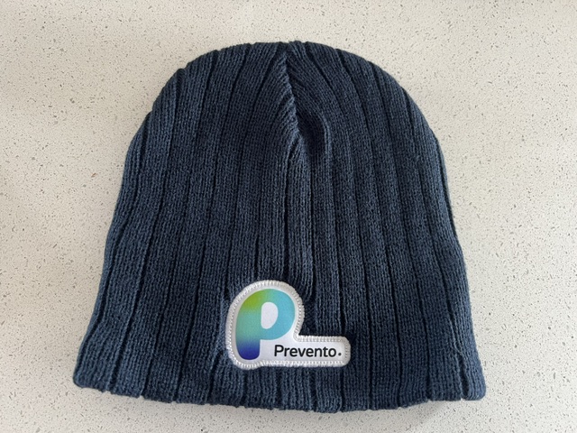 A dark knitted Prevento. beanie with logo patch sits on a light speckled Sydney surface.