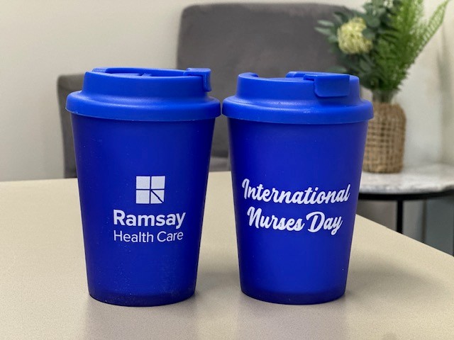Two blue reusable cups with Ramsay Health Care and International Nurses Day text, on a table indoors.