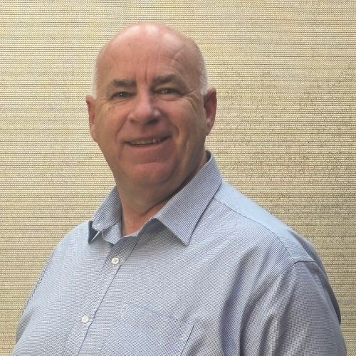 Smiling bald man in a light blue shirt—meet the team against a beige textured background.