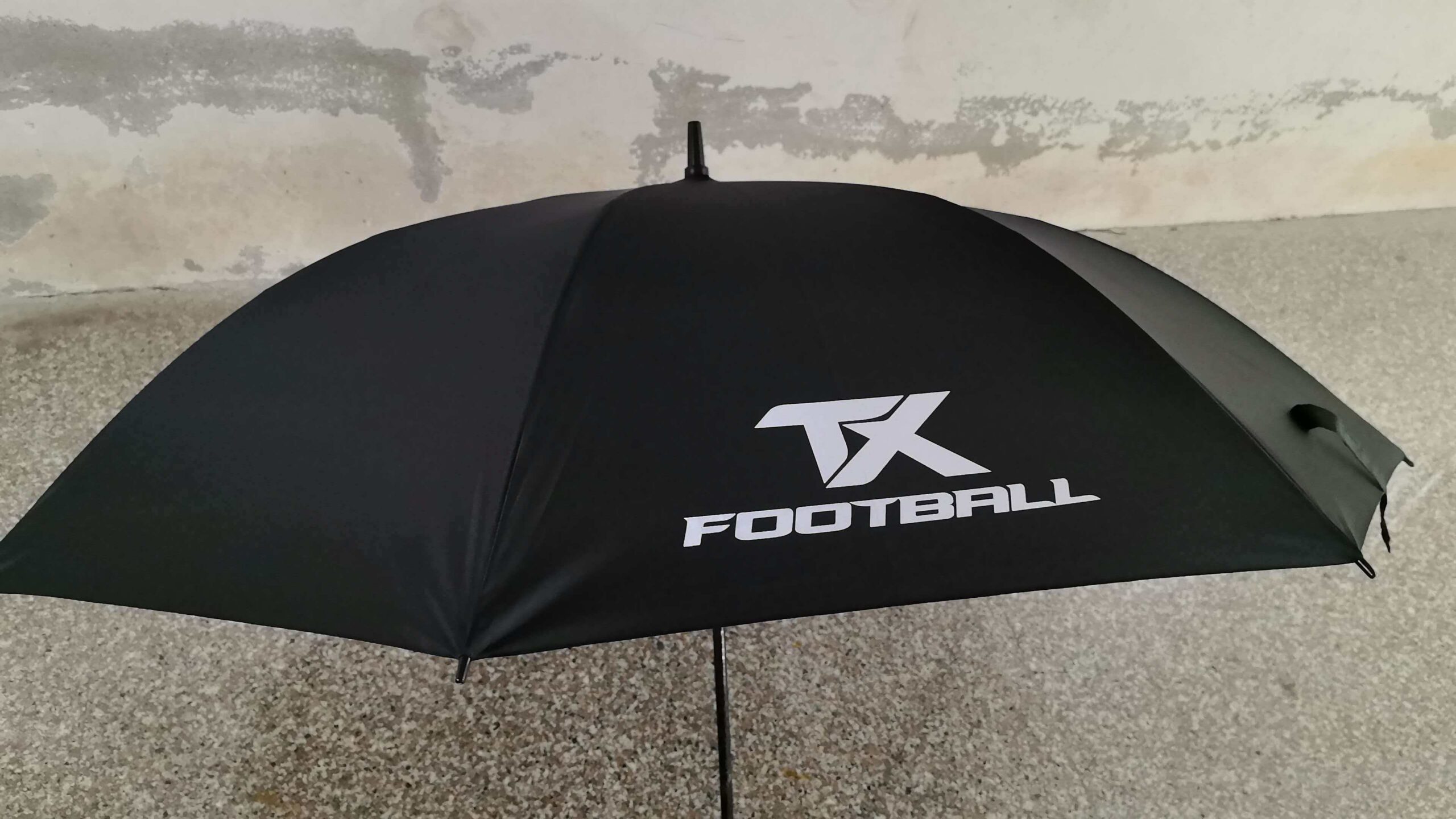 Black umbrella with TK FOOTBALL logo, set against a textured wall—Sports Group Melbourne.