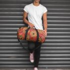 Man in white t-shirt holding colorful duffel bag, standing against metal shutter.