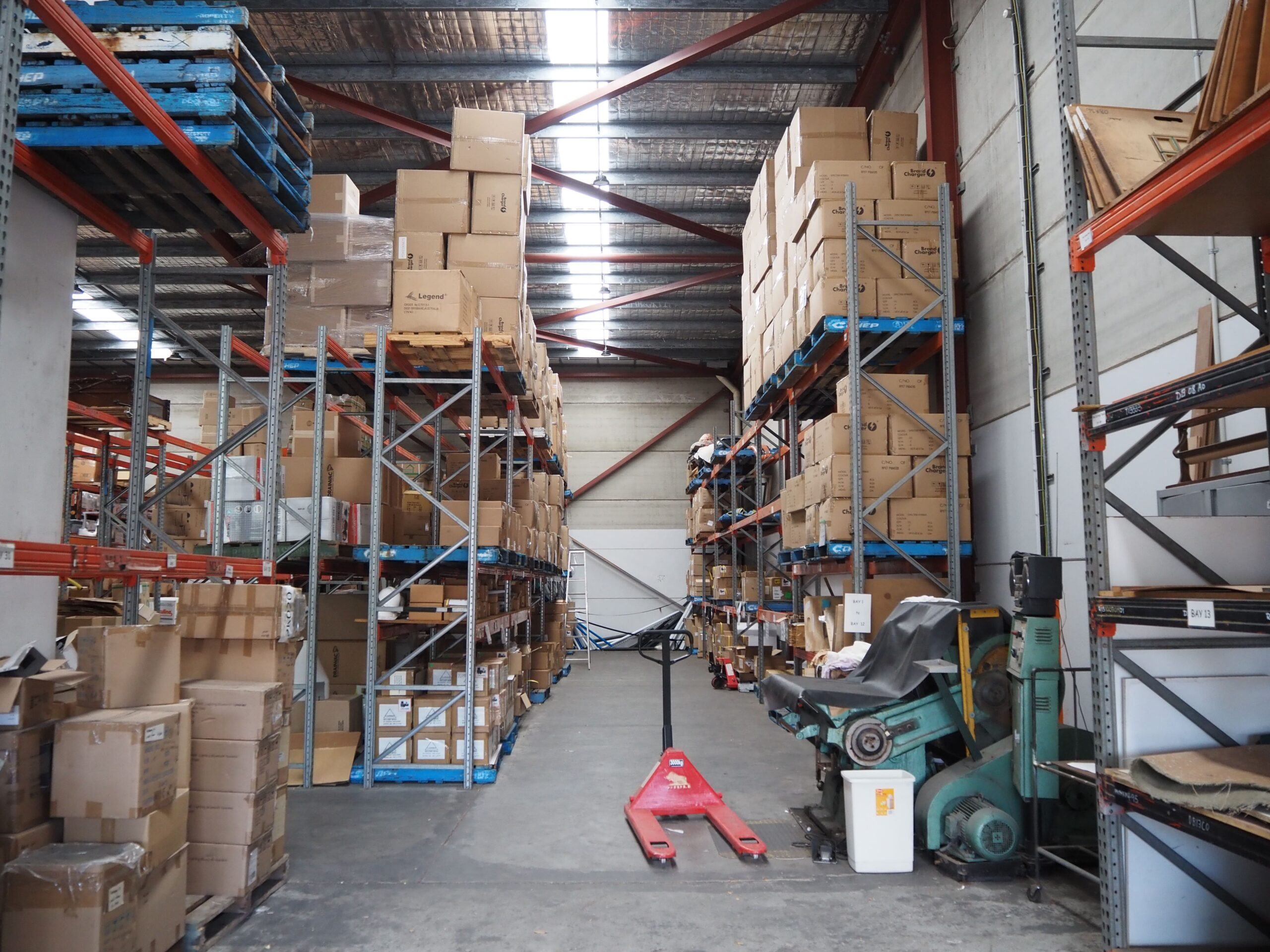 Warehouse interior with stacked shelves, red pallet jack, highlighting local production efficiency.