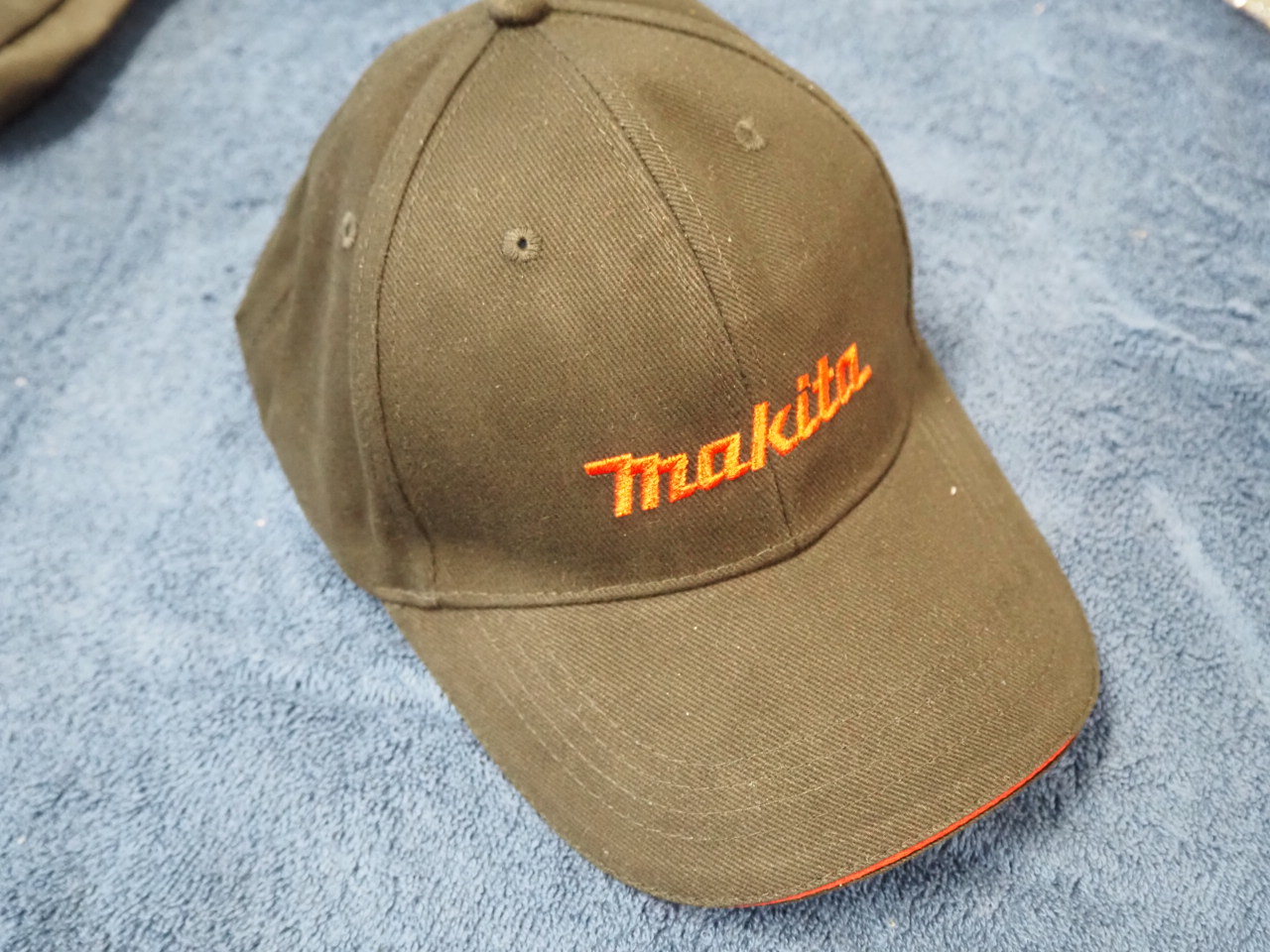 Black Makita baseball cap—great for car dealership giveaways—on a blue fabric surface.