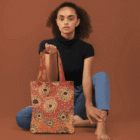 Woman in black top and blue jeans holding a patterned tote bag, sitting barefoot on floor.
