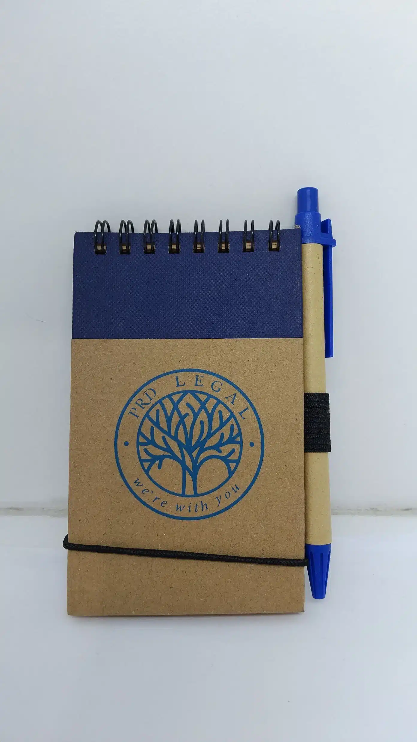 Small spiral notebook with a blue pen, tree logo, and PRD Legal—move with you.