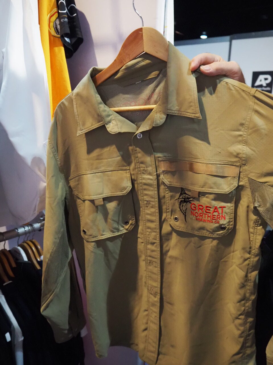 Khaki button-up shirt with expert-recommended logo placement, hanging on a wooden hanger.