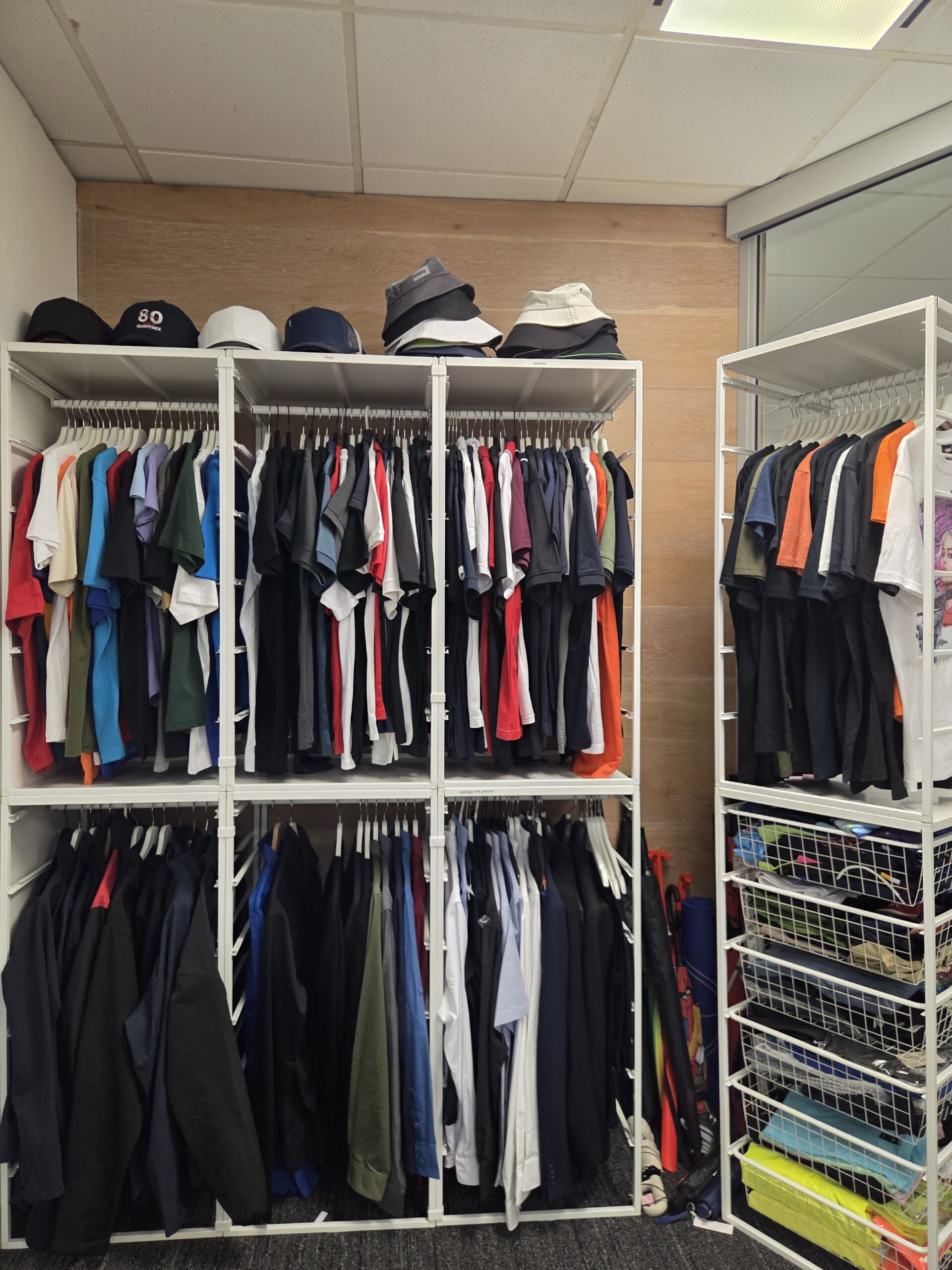 Colorful shirts and hats, perfect for uniform orders, neatly organized on white racks.
