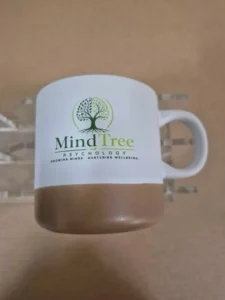 Two-tone ceramic coffee mug with white body and cork-style base, printed with MindTree Psychology logo across the front.