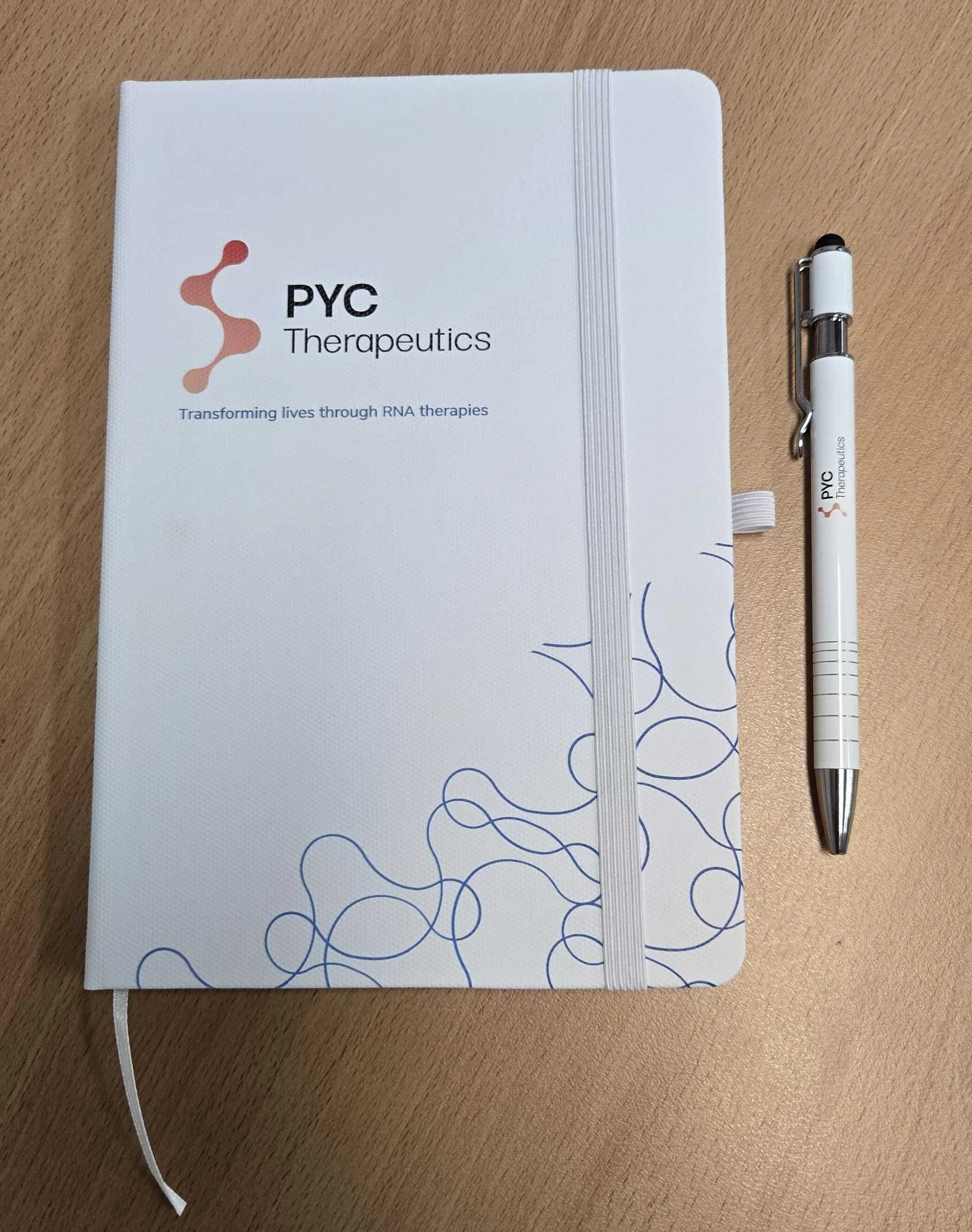 white notebook and pen branded with PYC Therapeutics logo