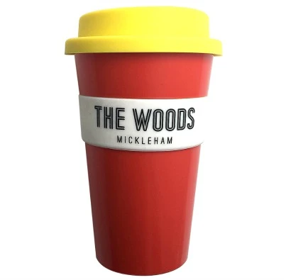 Red reusable cup with yellow lid, labeled THE WOODS MICKLEHAM on a white band.