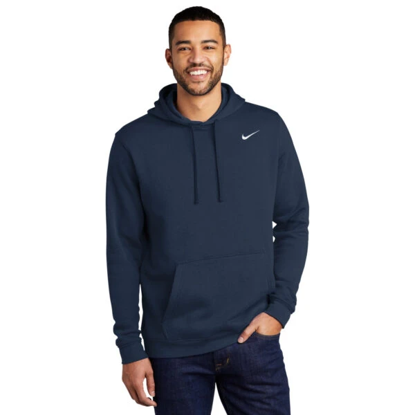 Man smiles in Nike Club Fleece Pullover Hoodie and jeans against a white background.