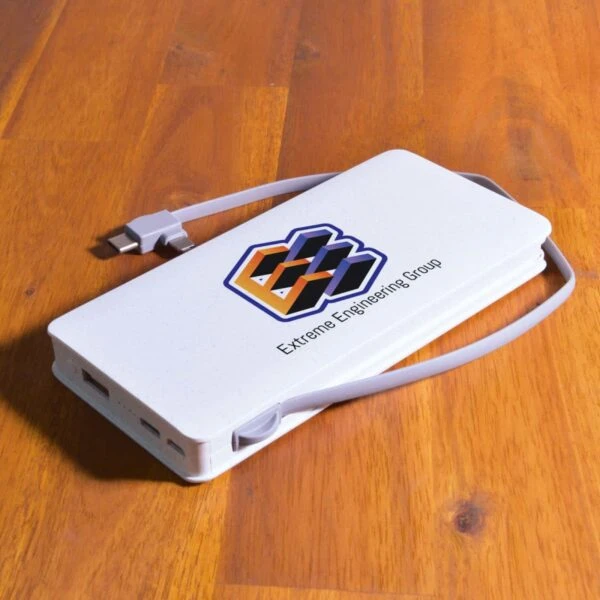 A white rectangular power bank with a gray charging cable rests on a wooden surface. The power bank features a colorful geometric logo and the text E-Xtreme Engineering Group.