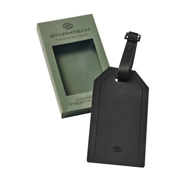 Black luggage tag with strap next to a green Stormtech box on a white background.