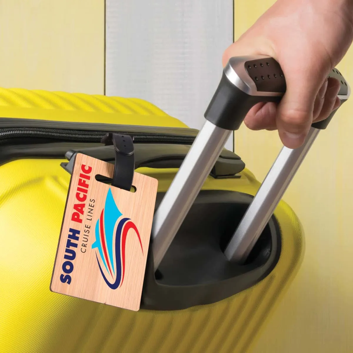 Hand pulling a yellow suitcase with a South Pacific Cruise Lines tag attached to the handle.