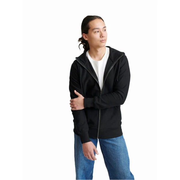 A person in a black Pure Waste Twill Jersey Zip Jacket and blue jeans stands against a white background.