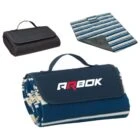 Folded picnic blanket with a carrying handle and ARBOK logo on top. Next to it, an open striped blanket showing its pattern, and a black folded blanket with a handle. The designs emphasize portability and outdoor use.