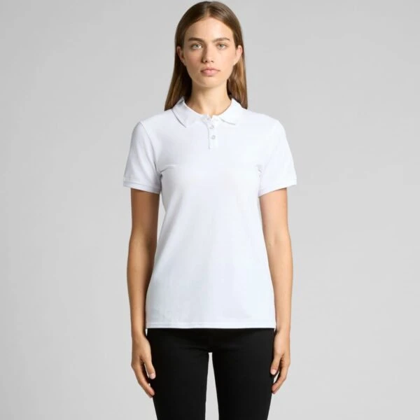 Woman wearing a plain white polo shirt and black pants, standing against a gray background.