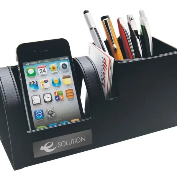A black desk organizer holding a smartphone, various pens, and a business card. The smartphone displays app icons on its screen. The organizer features a label with the text e-SOLUTION.