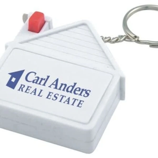 A keychain shaped like a house, featuring a red button and a metal key ring. The text on the house reads, Carl Anders Real Estate with a blue house logo.