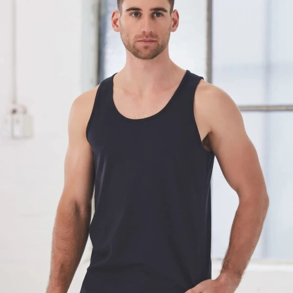 A man wearing a black tank top stands in front of a large window, looking at the camera. The background is a bright, minimalist room with some visible light fixtures.